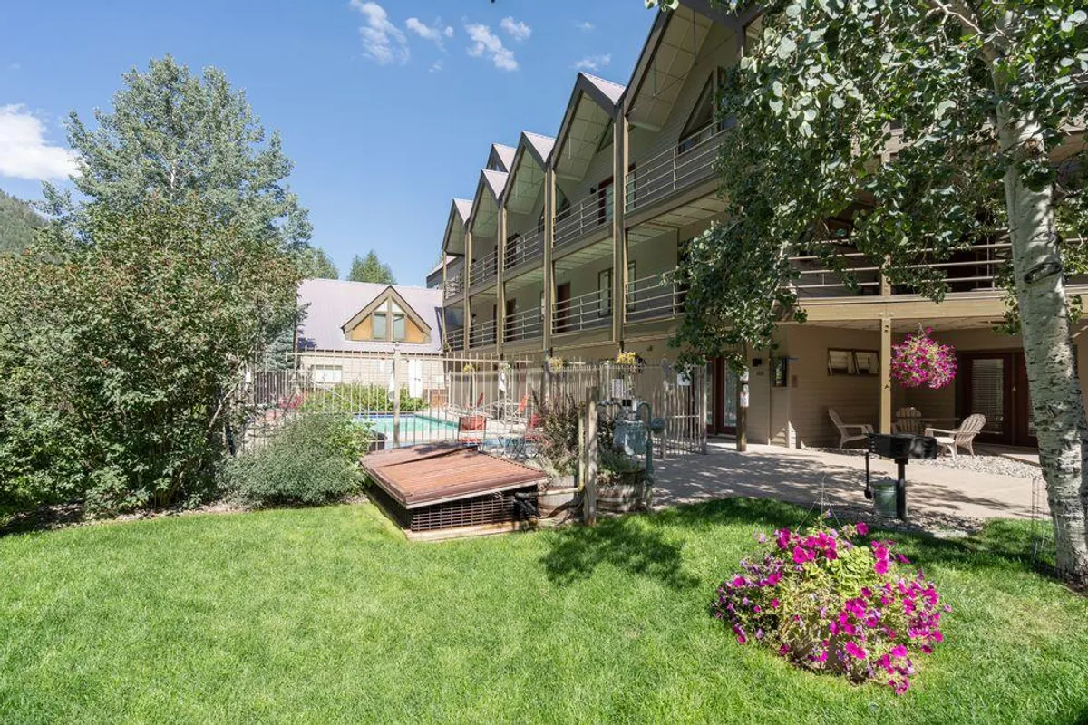This image features the outdoor swimming pool surrounded by flower beds, balcony areas, and attractive landscaping. The pool is a central communal amenity, ideal for swimming, sunbathing, and social gatherings, with sunny skies enhancing the resort-style ambiance.