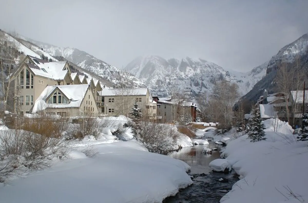 This image features snow-covered mountains, a winding river, and wooden buildings nestled into the landscape. The scene captures the essence of Telluride’s winter playground, with pristine snow offering opportunities for skiing, snowboarding, and winter hiking amid stunning natural surroundings.