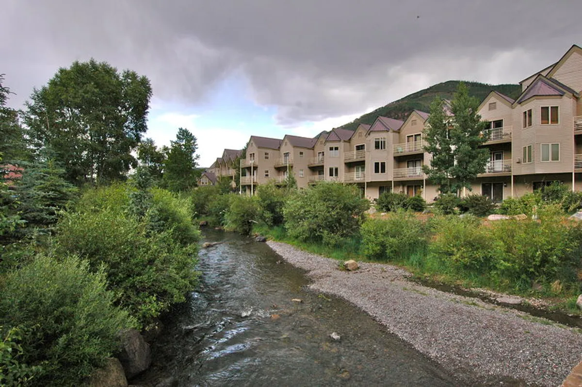 A tranquil view of the stream bordered by trees and buildings, offering a sense of peaceful riverfront access. The natural setting invites residents to stroll along the water's edge, enjoy nature walks, or simply relax with the sound of flowing water nearby.