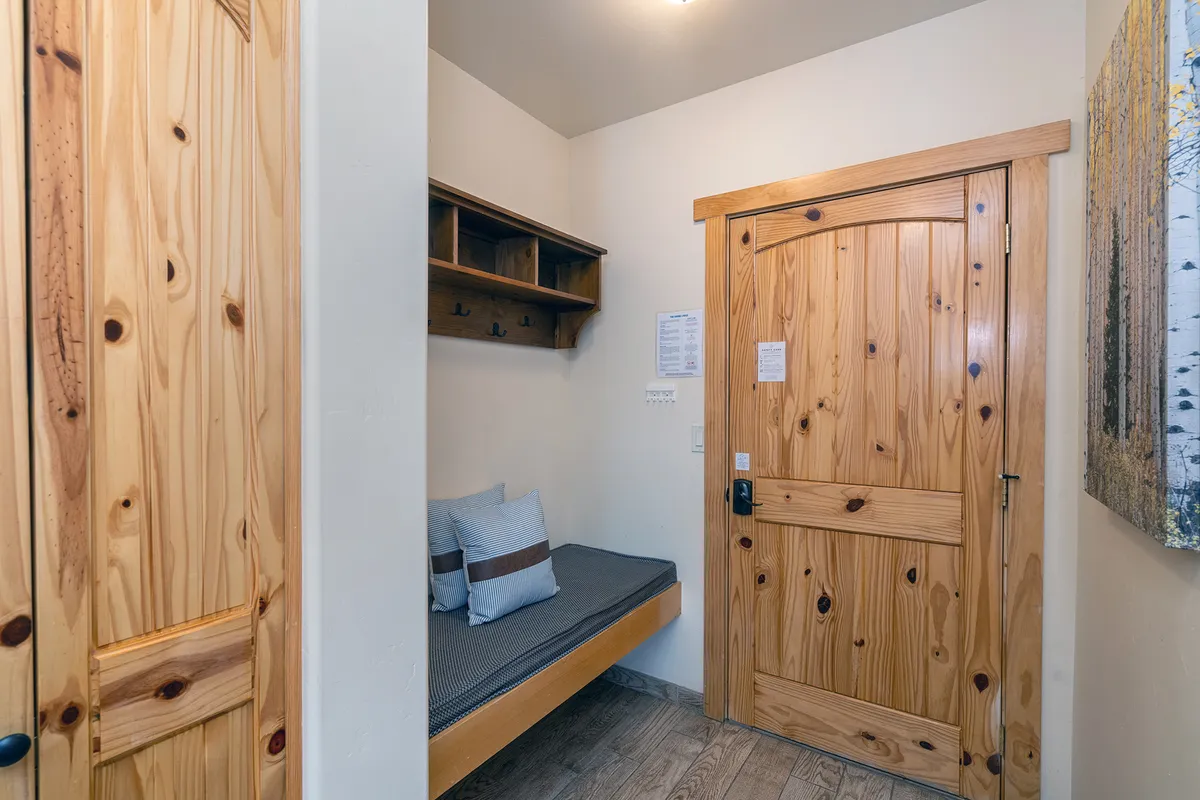 A compact entry nook with a wooden door, built-in bench seating, and shelves for storage. The setup is practical, inviting, and perfect for organizing outdoor gear or keeping personal items tidy.