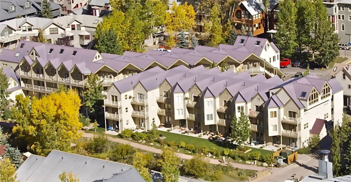 This image displays apartment buildings nestled among mature trees and landscaped gardens. The setting is tranquil and inviting, with balconies overlooking the foliage—evoking a sense of connection with the outdoors and the changing seasons. The presence of landscaping suggests ongoing property care and the kind of outdoor amenities referenced in the section.