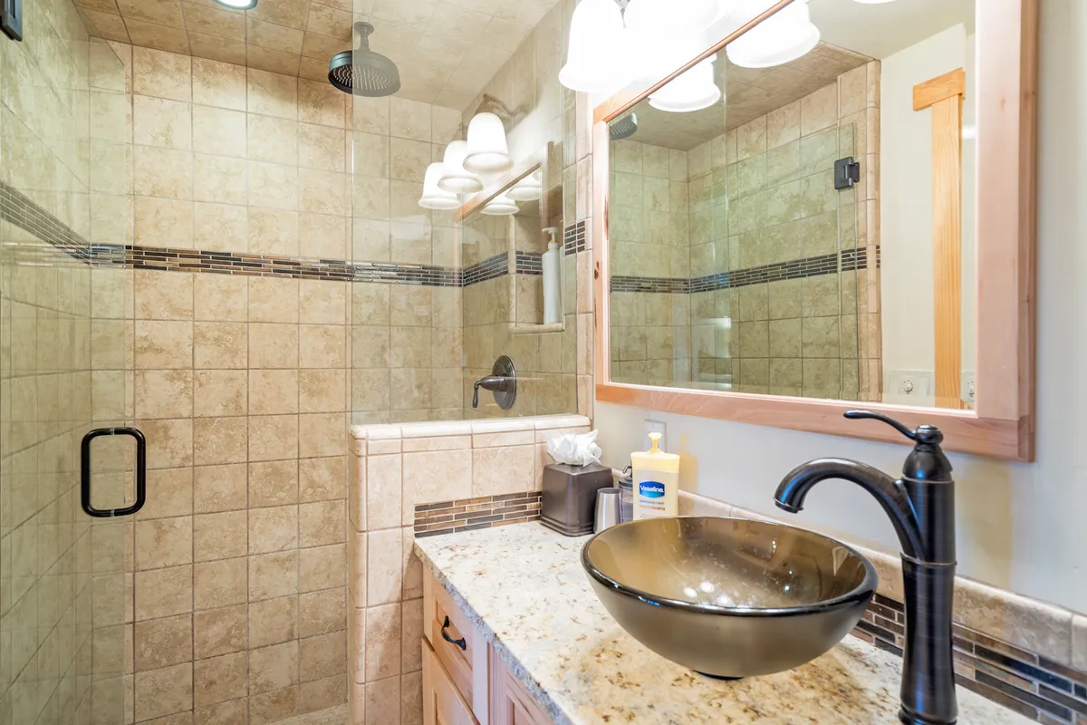A modern, updated bathroom interior with a glass shower enclosure, granite countertop, and contemporary sink and mirror. The clean, serene atmosphere underscores the comfort and convenience of the studio's amenities.